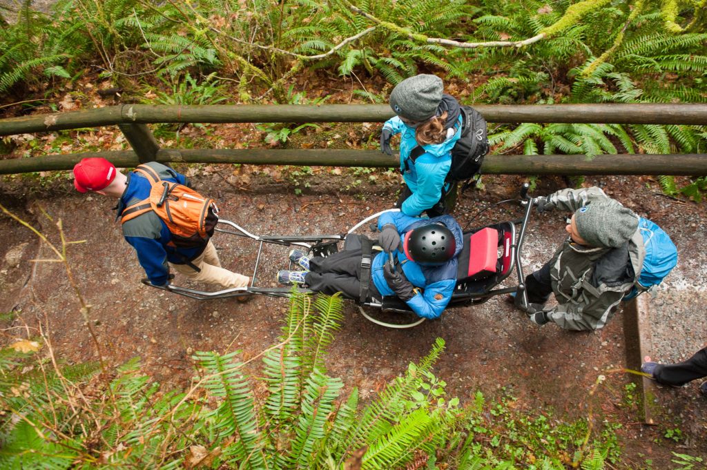 Hikers carrying a person with mobility issues on a trail in the woods.